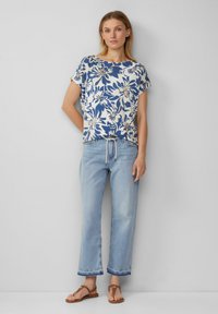 Top à imprimé floral bleu et crème, à manches courtes, avec une coupe décontractée. Associé à un jean large à délavage clair et des sandales marron.