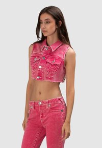 Różowa krótka kurtka dżinsowa z kołnierzykiem, przednimi kieszeniami i srebrnymi guzikami; zestawiona z różowymi spodniami dżinsowymi z wysokim stanem o postarzanym wykończeniu.