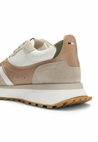 Sneaker beige e crema realizzata con materiali in suede e pelle. Presenta una suola in gomma, una parte superiore testurizzata e il marchio sul tallone.