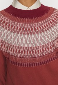 Sweter z dzianiny w kolorach bordowym i jasnoczerwonym, z teksturowanym, geometrycznym wzorem w okolicy dekoltu oraz ściągaczem.