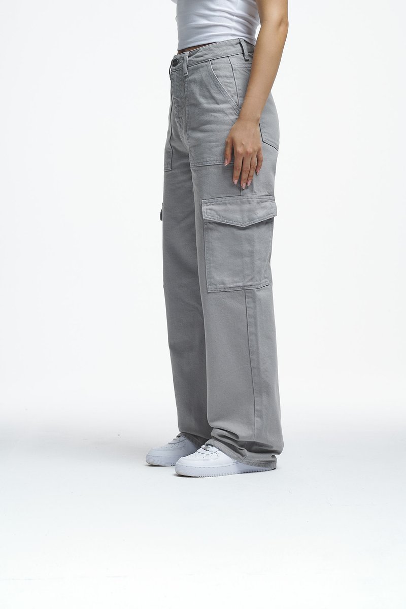 Pantalones cargo grises hechos de una mezcla de algodón, con grandes bolsillos laterales, corte recto y detalles de costura, acompañados de zapatillas blancas.