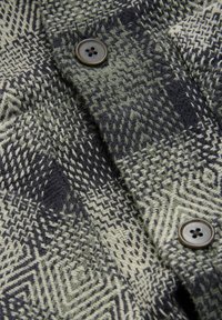 Gros plan d'un manteau en laine gris et noir à motifs avec deux boutons foncés et un tissu tissé texturé.