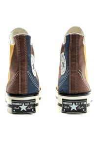 Höga sneakers med blandade paneler i brunt, blått och gult kanvastyg, vit söm, logotyppatch, svart sula och vita stripe-accenter.