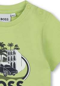 Maglietta in cotone verde chiaro a maniche corte, con una grafica illustrata di un edificio e un'auto, arricchita da dettagli in bianco e nero.