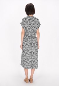 Rochie midi floral�ă în alb și negru, cu talie strânsă, mâneci scurte și o croială lejeră, asociată cu pantofi cu toc bloc bej.