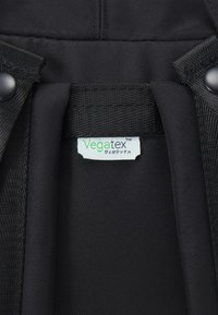 Zwarte stof met een glad, gestructureerd oppervlak; heeft een zichtbare label met de tekst "Vegatex™" in groen en wit. Geen aanvullende details of patronen.