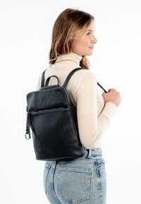 Svart läderryggsäck med strukturerad yta, övre handtag och justerbara remmar. Har en framficka med dragkedja för enkel åtkomst.