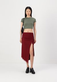 Grønn ribbet crop top sammen med en burgunder rynket maxi skjørt med høyt slitt. Svarte ankelstøvler fullfører antrekket.
