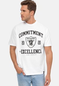 Camiseta de algodón blanca con texto impreso en negro "COMPROMISO CON LA EXCELENCIA" y "RAIDERS", con un diseño gráfico de escudo.
