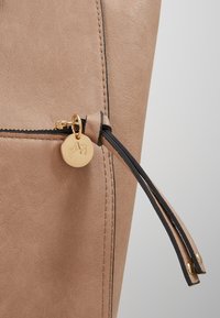 Borsa in ecopelle beige con texture, dotata di zip dorata con un ciondolo circolare e dettagli in zip nera a contrasto.