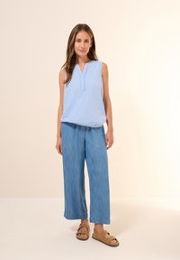 Haut sans manches rayé bleu clair avec un décolleté en V, associé à un pantalon en denim à jambes larges. Des sandales marron complètent la tenue décontractée.
