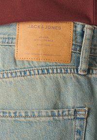 Hellblaue Denim-Jeans mit einem braunen Lederetikett, das geprägten Text aufweist. Das Etikett ist in den Bund eingenäht und hebt die Markendetails hervor.