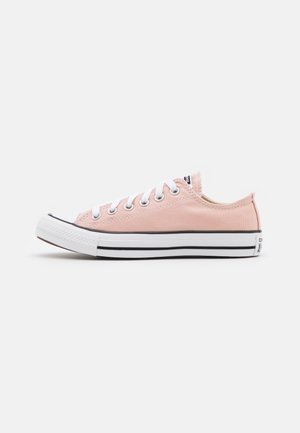 Zapatilla baja de lona rosa con cordones blancos, puntera de goma blanca y suela blanca con rayas negras, mostrada de lado.