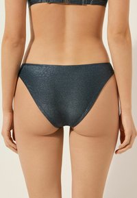 Ciemnoniebieskie majtki od bikini z teksturowanym wzorem przypominającym skórę krokodyla. Wysoki krój z umiarkowanym przykryciem i gładkimi liniami.