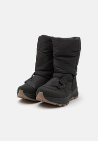 Sorte isolerte støvler med en puffy overdel, sikret med svarte elastiske stropper, med en solid grønn såle med et teksturert mønster.