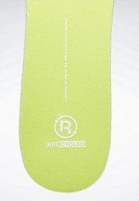 Grön skoinlägg gjort av återvunnet material, med en texturerad yta och en cirkulär logotyp med "ÅTERVUNNEN" under.