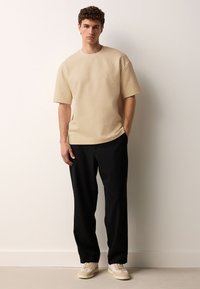 Beige short-sleeve textured shirt paired with black pants and light-colored sneakers. Simple design with relaxed fit and round neckline.