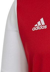 Rote und weiße Sporttrikot aus strukturiertem Stoff. Verfügt über ein auffälliges weißes Adidas-Logo auf der Brust. Kurze Ärmel mit modernem Design.