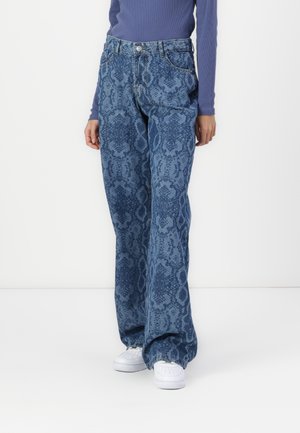 Blue wide-leg jeans with a snake skin pattern in varying shades, featuring front pockets and a button closure. Worn with white sneakers.