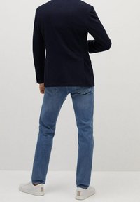 Granatowa marynarka, jasnoniebieskie dżinsy, białe buty z beżowymi akcentami. Marynarka ma dopasowany krój i jedno tylne rozcięcie, dżinsy mają tapered fit.