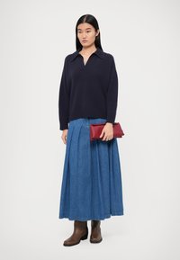 Navy knitted sweater with a V-neck, paired with a long denim skirt. The outfit is accessorized with a red clutch and brown ankle boots.