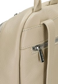 Beżowy skórzany plecak z teksturowaną powierzchnią, z przednią kieszenią na zamek błyskawiczny i srebrnymi akcentami. Posiada dwie górne rączki do noszenia.