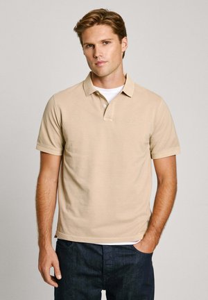 Polo de color beige hecho de algodón, de mangas cortas, con una tapeta de dos botones y un detalle de logo sutil en el pecho. Combinado con jeans oscuros.