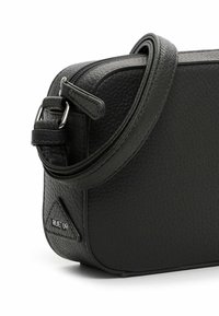Černá kožená crossbody taška s texturovaným povrchem, zipovým uzávěrem, nastavitelným popruhem a trojúhelníkovým logem po straně.