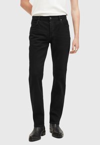 Jeans de mezclilla negra, corte recto, con cinco bolsillos, cierre de botón y detalles de costura sutiles. Combinados con botas negras hasta el tobillo.