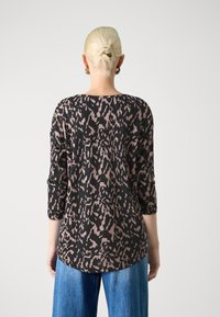 Black and beige leopard print top with three-quarter sleeves, round neckline, and a relaxed fit, paired with blue wide-leg jeans.