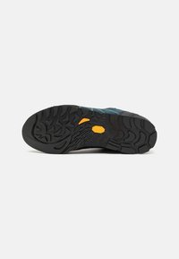 Semelle de chaussure d'extérieur avec une surface en caoutchouc noir robuste, de profondes rainures pour l'adhérence, et un accent orange vif près du centre.