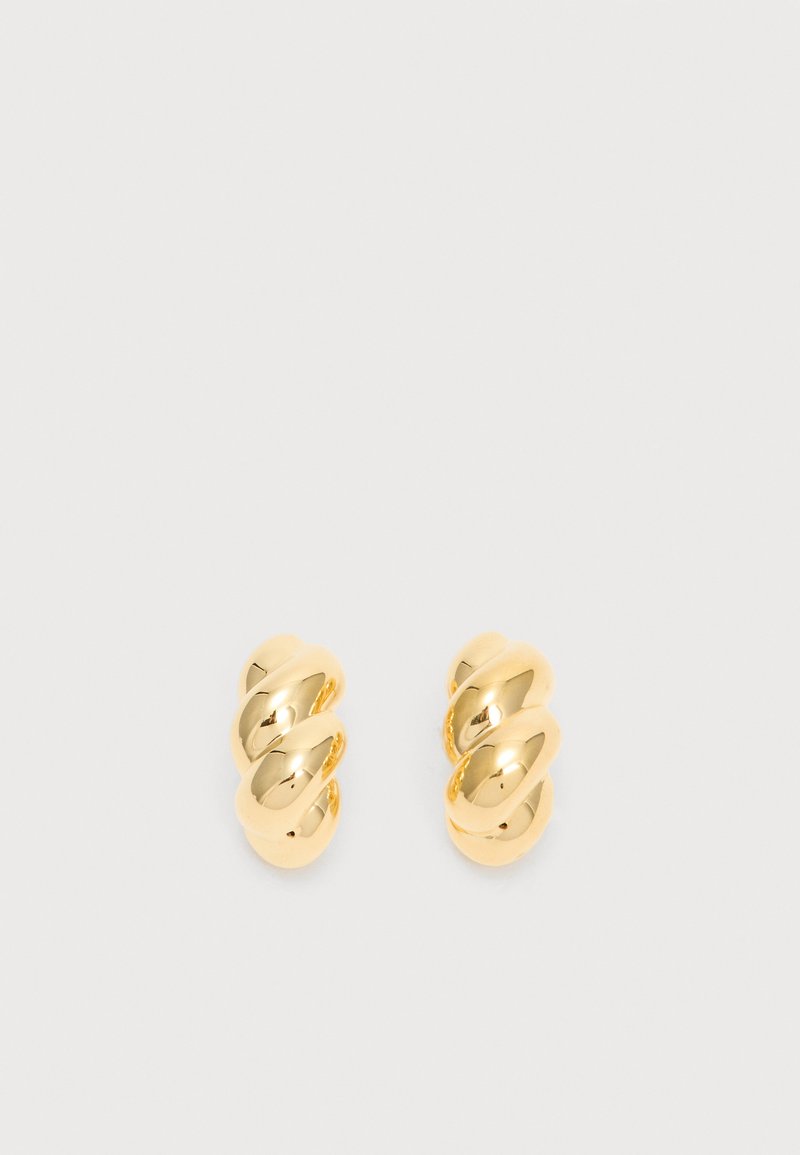 Ζευγάρι λαμπερών χρυσών στριφογυριστών κρίκων σκουλαρικιών σε απλό φωτεινό φόντο, που δείχνει αντανακλαστική γυαλισμένη μεταλλική επιφάνεια.