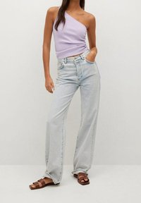 Lilac one-shoulder toppi, jossa on poimutus yksityiskohtana, yhdistettynä vaaleansinisiin leveisiin farkkuihin ja ruskeisiin hihnakenkiin. Suuri kangasrakenteen pehmeys.