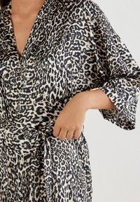 Leopardprint morgenkåbe med en silkeagtig tekstur, kimonoærmer, en båndlukning i taljen og en v-halsdesign i beige og sorte nuancer.