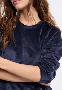 Granatowy welurowy sweatshirt z wypukłym wzorem serca. Okrągły dekolt, długie rękawy z marszczeniami na mankietach.