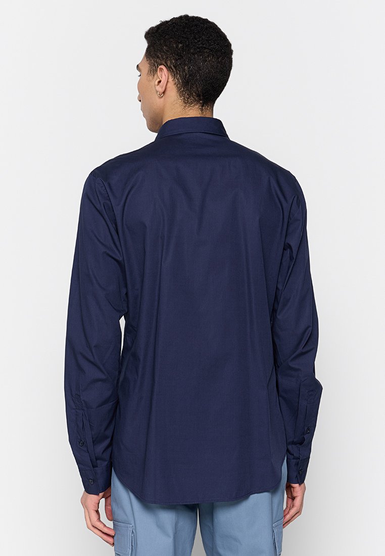 Chemise à manches longues marine à coupe droite, avec des poignets à boutons et un col classique. Texture de tissu lisse sans motifs ni accents visibles.
