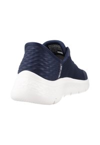 Marinblå träningssko med texturerat mesh-ovandel, mjuk vit sula och rundad häl. Har en elegant design och minimal varumärkesprofil.