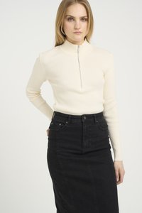 Maglione a coste di colore crema con collo alto e chiusura frontale a mezza zip. Abbinato a una gonna in denim nera a vita alta, con tasche.