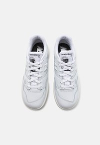 Weiße Ledersneaker mit runder Zehenpartie, featuring ein strukturiertes Design, flache weiße Schnürsenkel und ein schwarzes Logo auf der Zunge. Die Sohle ist cremfarben.