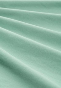 Tela de algodón verde claro exhibida en suaves pliegues fluidos, mostrando una textura suave y un sutil patrón de estriado en todo su superficie.
