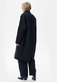 Zwarte jas met een ontspannen pasvorm, lange mouwen en zijzakken, gecombineerd met donkere jeans en geklede enkellaarzen. Gladde textuur en op maat gemaakt ontwerp.