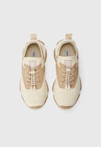 Krem- og beige joggesko med en teksturert mesh-overdel, kontrasterende glatte detaljer, snøring og en løkke på hælen.