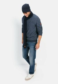 Navy gestrickter Pullover mit geripptem Kragen, passendem Schal und Mütze. Kombiniert mit hellblauen Jeans und weißen Sneakers. Strukturiertes Material.