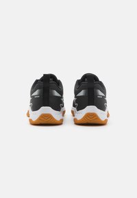 Chaussures de sport noires avec une tige en mesh, semelle intermédiaire blanche et semelle extérieure en caoutchouc orange. Équipées d'une languette de traction et d'accents réfléchissants sur les côtés.