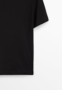 T-shirt noir en coton à manches courtes avec un ourlet simple sur un fond blanc uni, montrant uniquement le côté droit.
