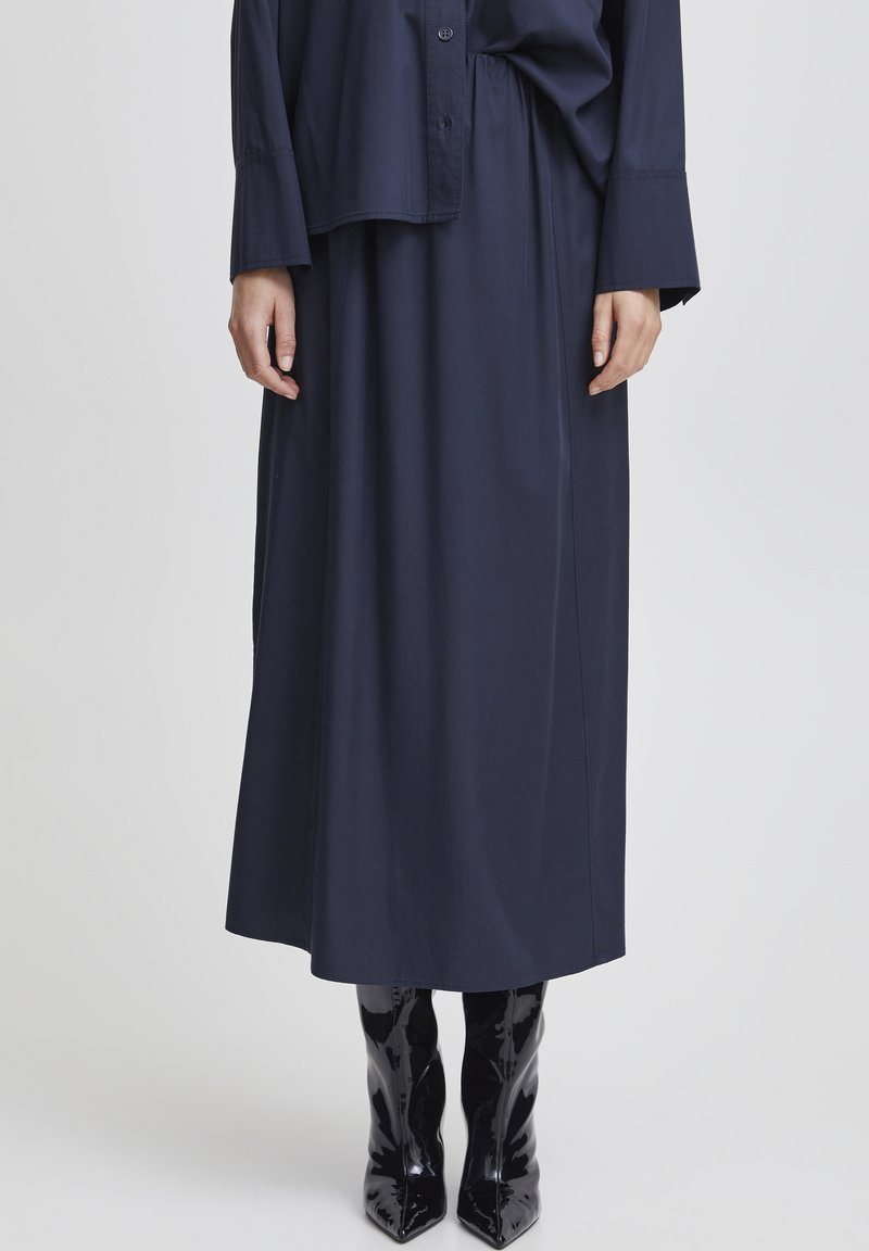 Robe longue bleu marine avec une coupe décontractée, dotée d'un devant boutonné, de manches à revers et d'une taille haute ; associée à des bottes noires brillantes jusqu'au genou.