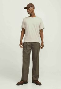 Beige t-shirt med klassisk rund hals, som kombineras med löst passande olivgröna byxor och bruna skor. En brun keps fulländar looken.