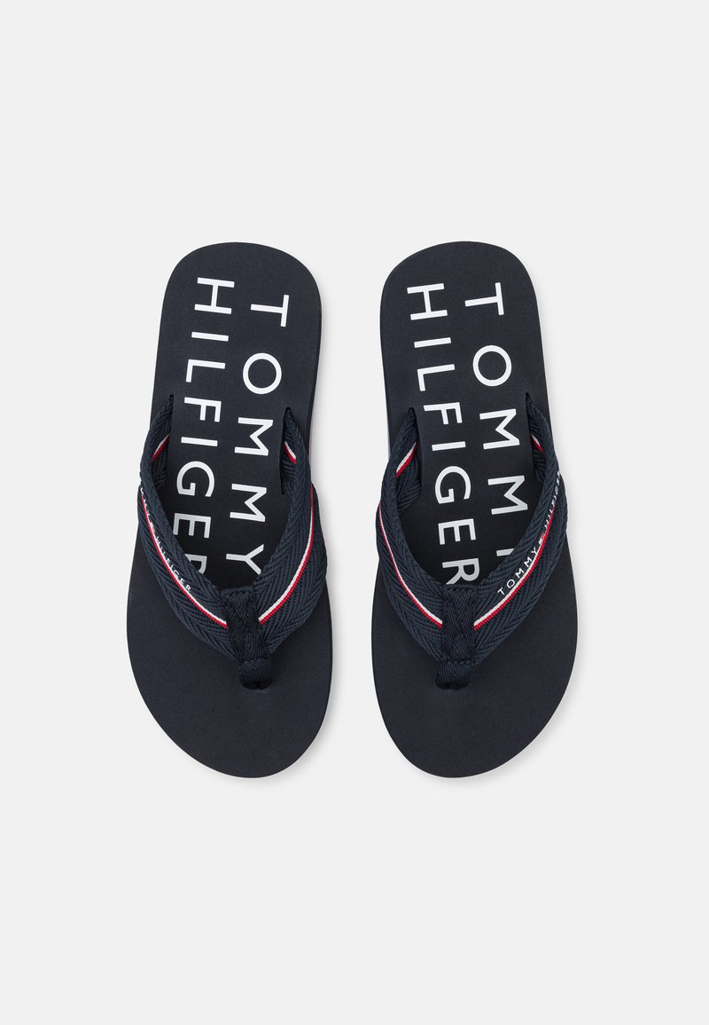 Sandale de plajă bleumarin cu un brad texturat, prezentând accente roșii și albe. Tălpița afișează "TOMMY HILFIGER" în litere albe, îndrăznețe.