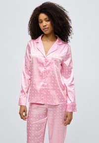 Rosa Satin-Pyjama-Set mit langärmligem Oberteil und Hose. Dezente Herzmuster und eine Tasche mit dekorativem Design. Glatte Textur.