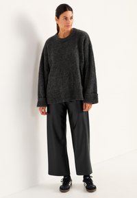 Donkergrijs oversized sweater met ribgebreide manchetten en zoom, gecombineerd met zwarte wijde broek en zwarte sneakers. Glad textuur, minimalistisch ontwerp.